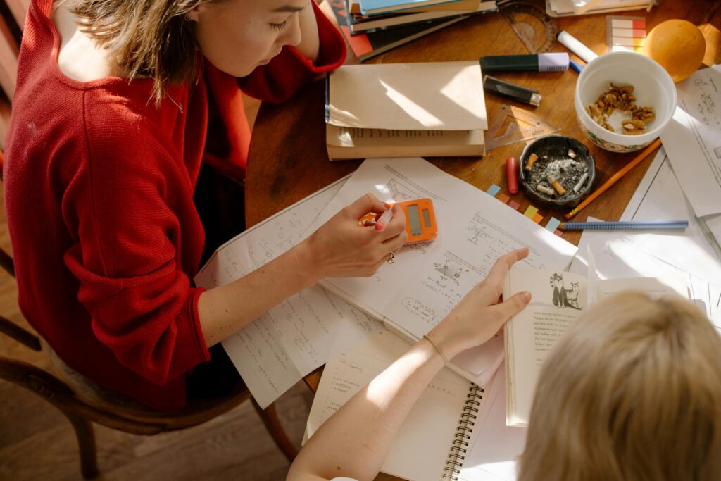 pexels-photo-4778660-4778660 Two students engaged in studying at a table with textbooks, notes, and stationery.